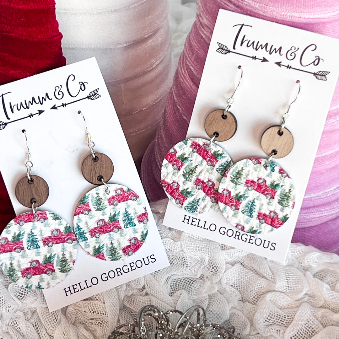 Circle leather Christmas earrings with red pick up truck and pine tree along with wood accents, leather earrings on a Trumm & Co earring card