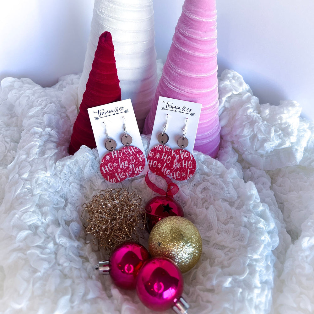 Christmas scene with red leather earrings, white lettering saying ho ho by ornaments and velvet trees