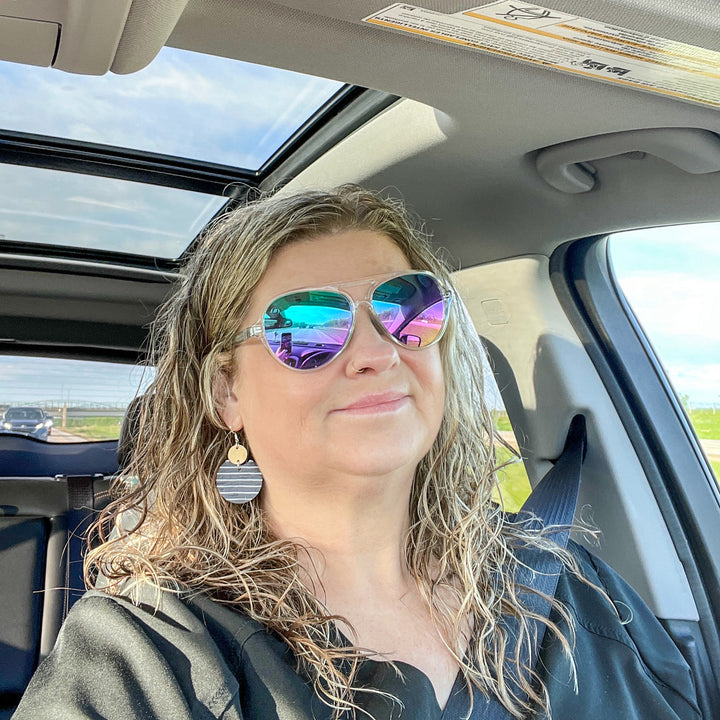 woman in a car wearing sunglasses in her car showing her pari of earrings