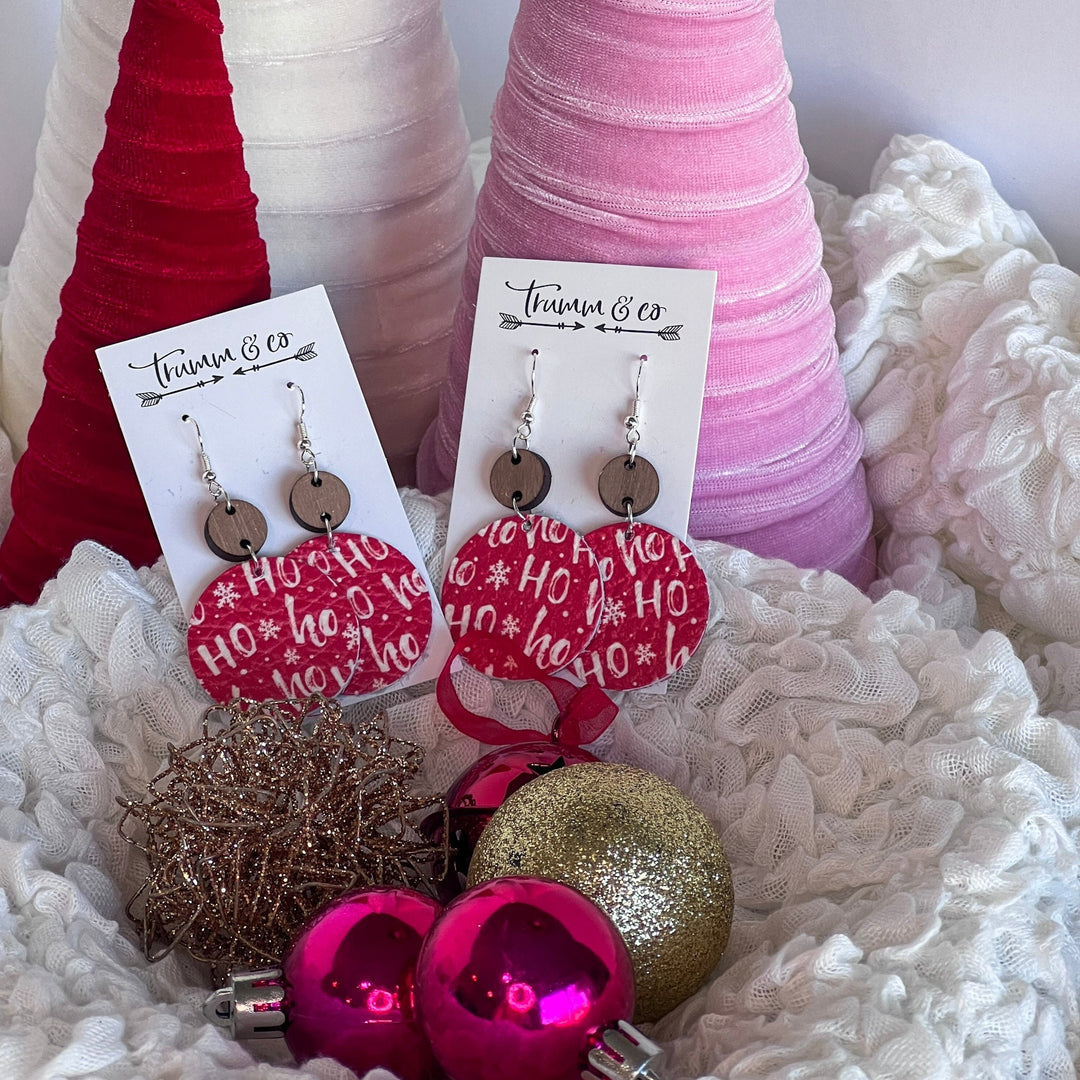 Christmas leather earrings that say hoho on them and laying on puffy white, with velvet trees and ornaments